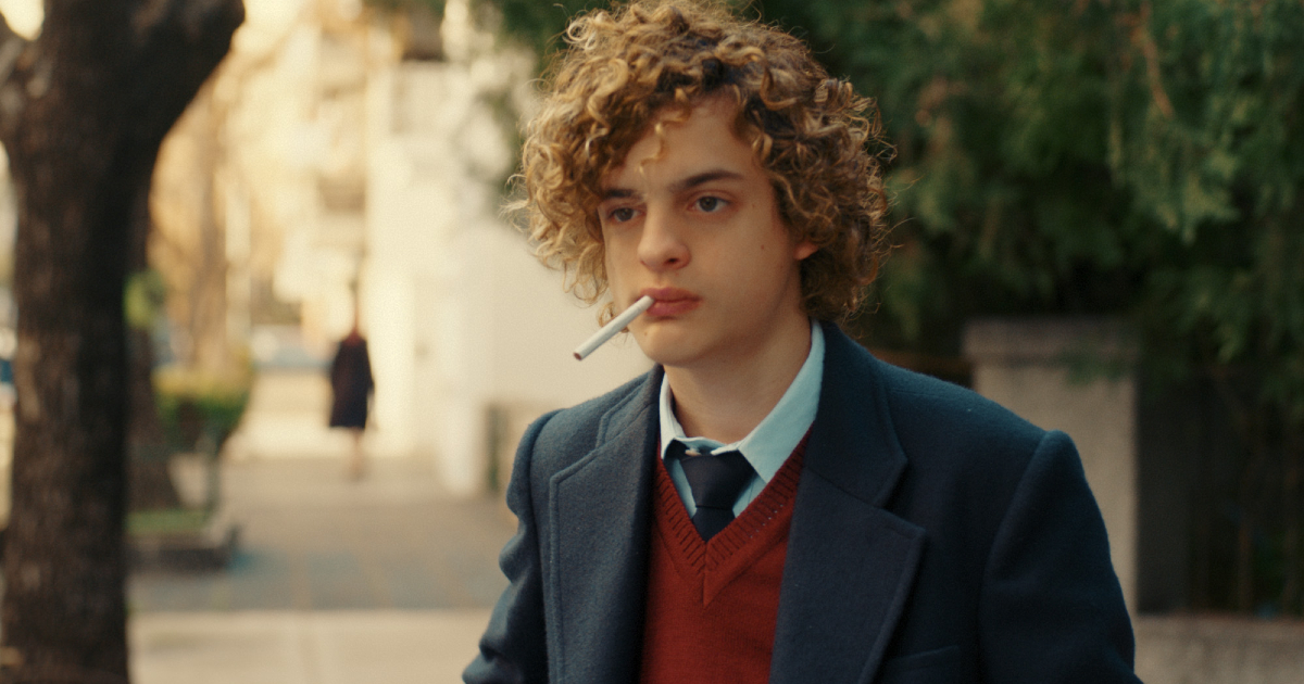 un giovane carlitos sta con una sigaretta in bocca e vestito con la divisa della scuola - nerdface