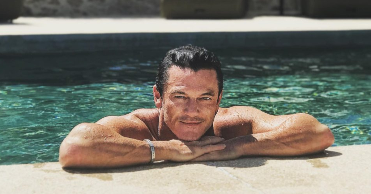 luke evans è immerso in una piscina ma si tiene ai bordi sulle braccia e sorride - nerdface