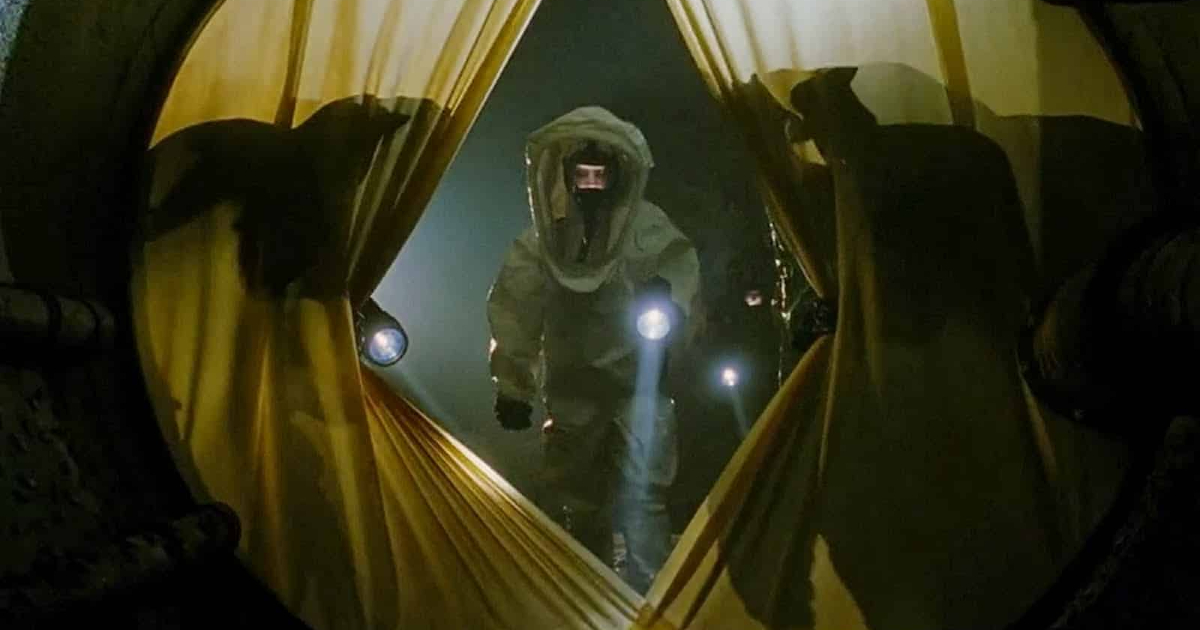 un uomo in tuta anti radiazioni con una torcia entra in una sala coperta da una tenda in mimic - nerdface