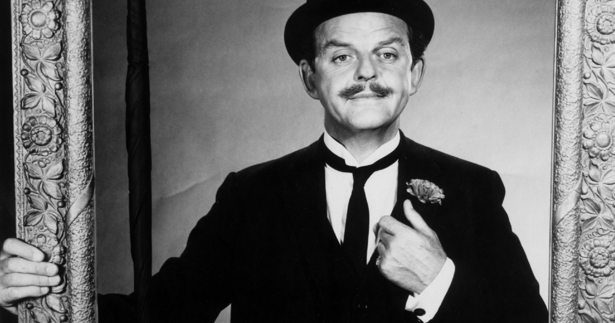 david tomlinson si aggiusta il cravattino mentre tiene una cornice in mano - nerdface