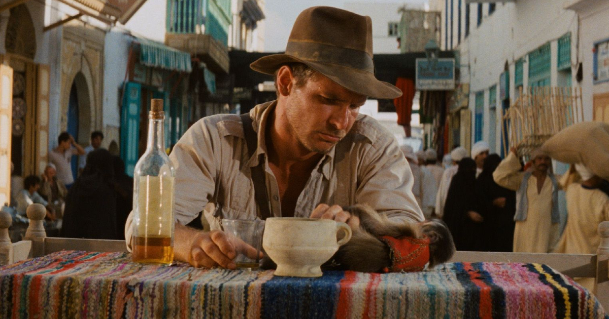 in indiana jones e i predatori dell'arca perduta harrison ford è seduto da solo al tavolo di un suk - nerdface