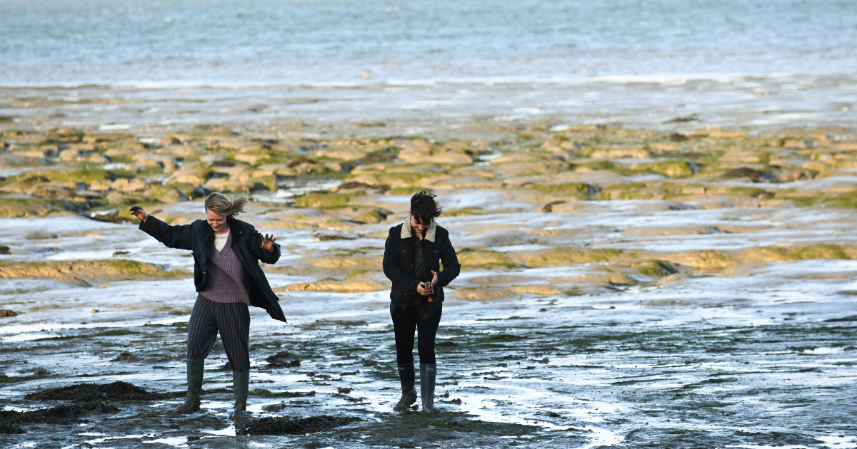 due protagonisti del film camminano e ridono su una secca del mare - nerdface