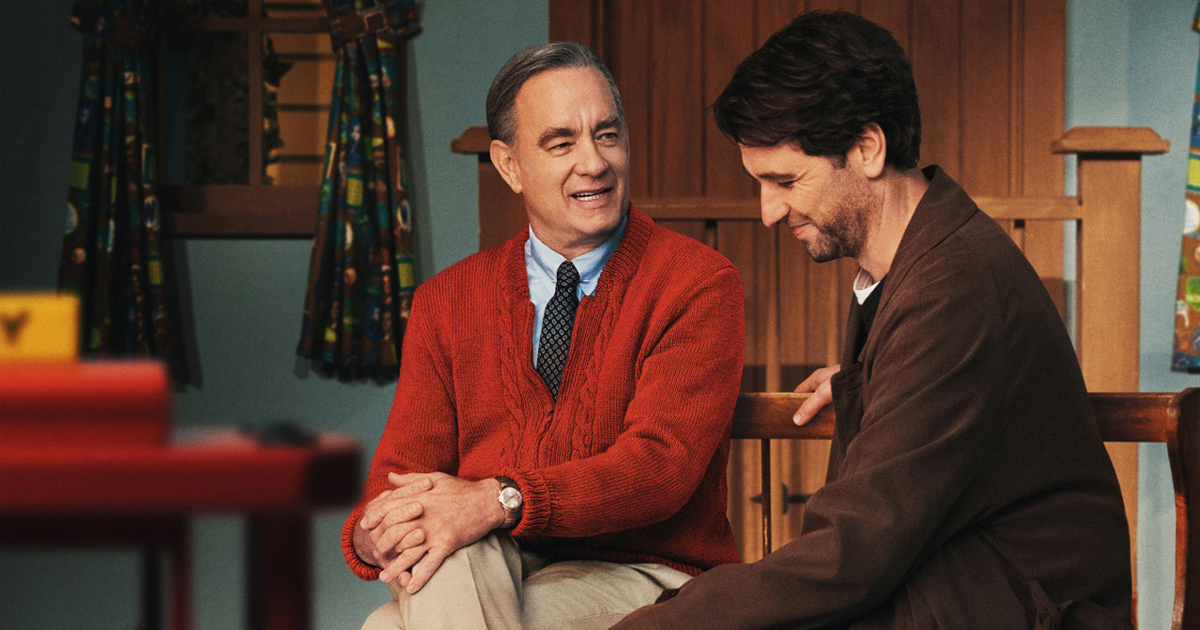 tom hanks interpreta fred rogers e siede accanto al giornalista che lo deve intervistare, entrambi sorridono - nerdface