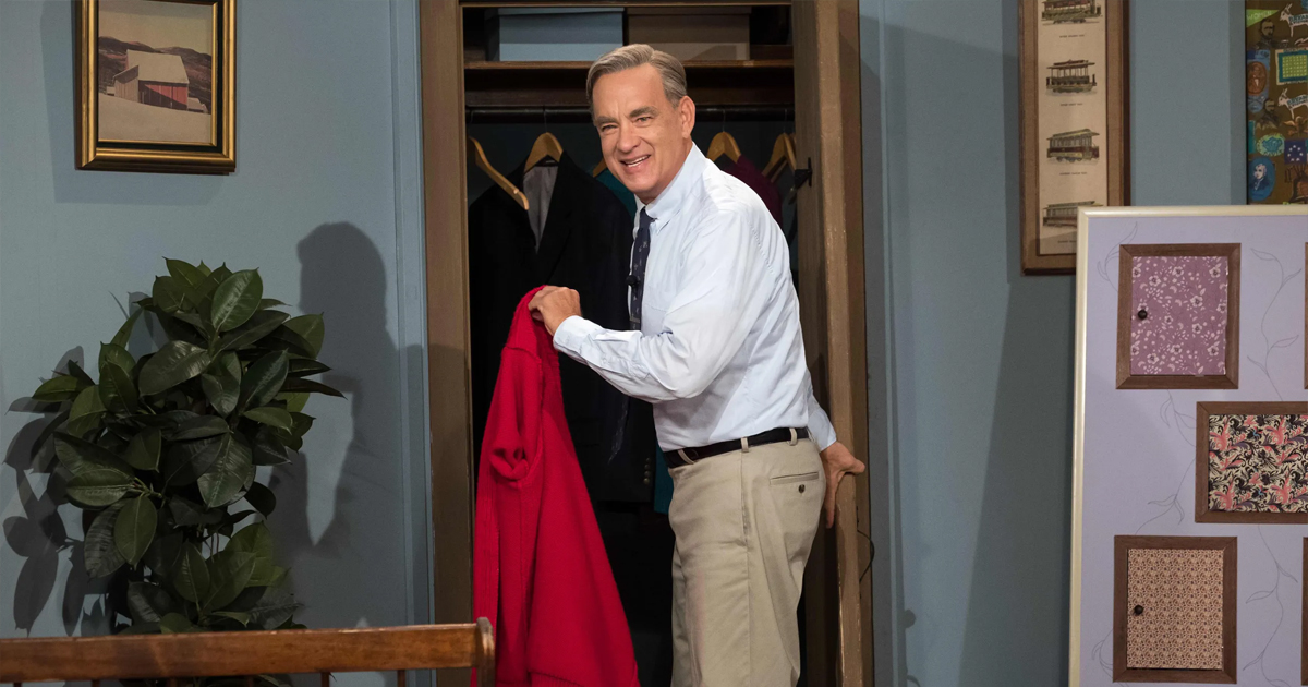 tom hanks è fred rogers, tiene la sua giacca rossa con la mano e si volta sorridendo verso qualcuno in un amico straordinario - nerdface