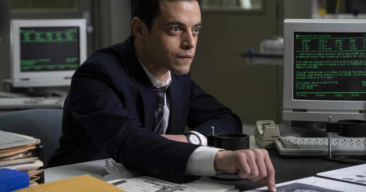 rami malek è alla scrivania e sembra mo,to determinato mentre parla con qualcuno - nerdface