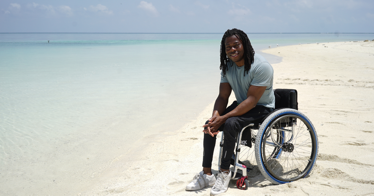 Ade Adepitan sorride su una spiaggia bianca e deserta - nerdface