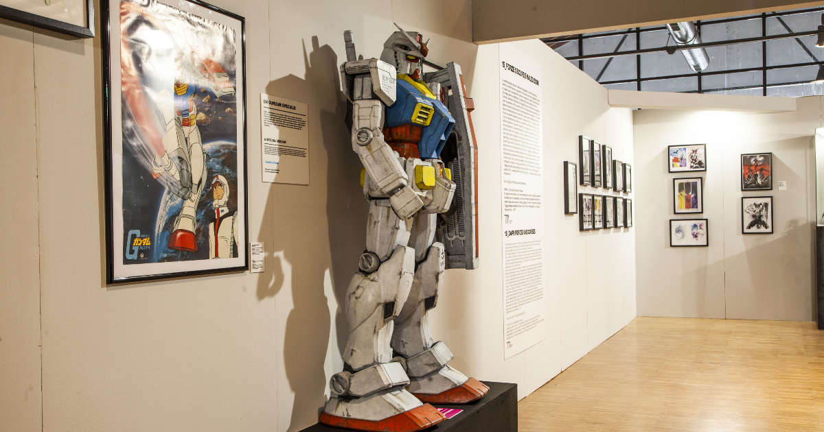 una statua di gundam esposta accanto a un manifesto dell'anime - nerdface