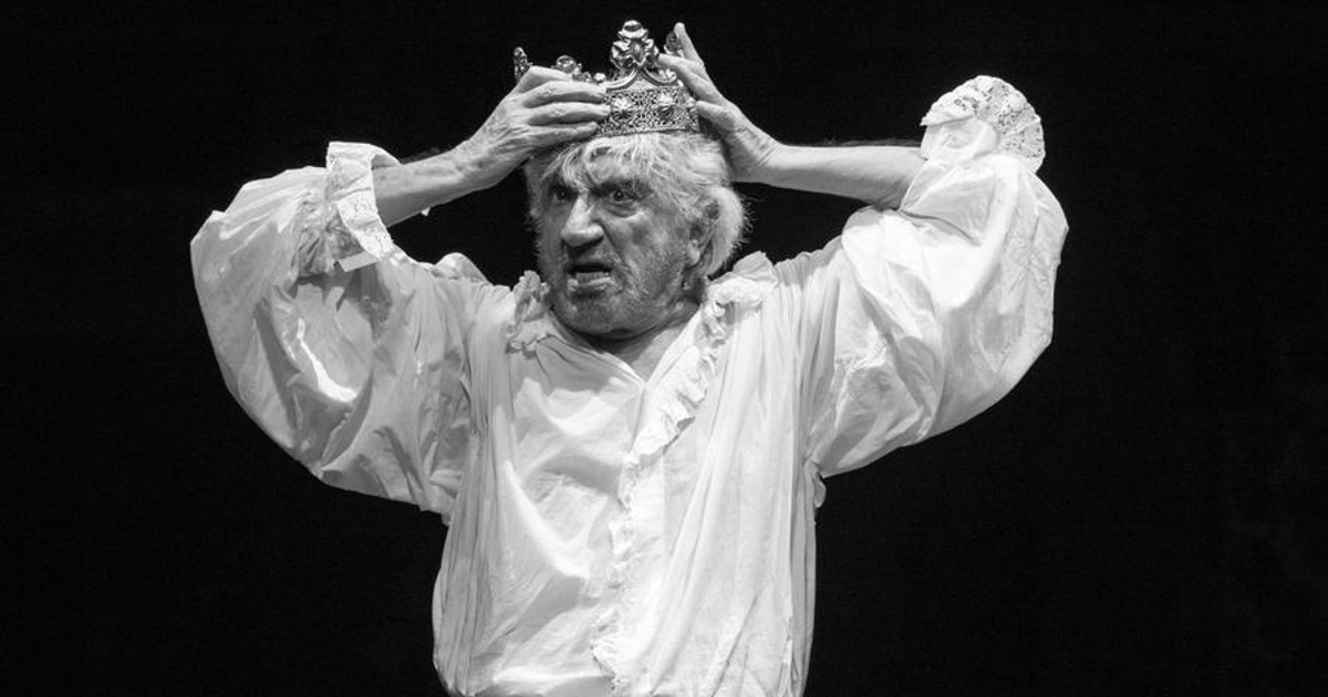 un gigi proietti già anziano indossa una corona durante uno spettacolo teatrale - nerdface