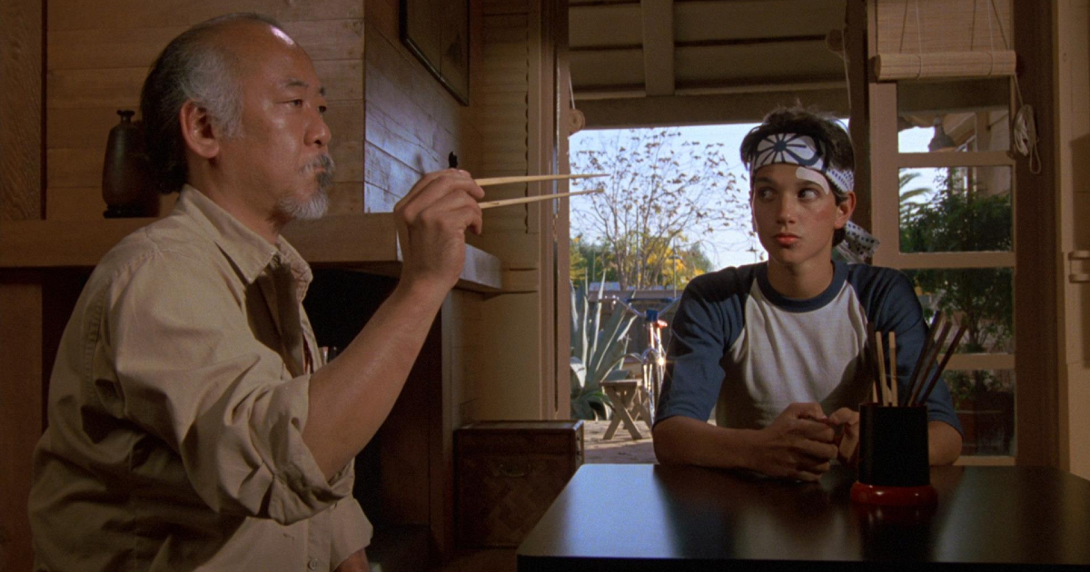 il maestro miyagi tenta d'afferrare una mosca con le bacchette in karate kid, davanti un esterrefatto ralph macchio - nerdface