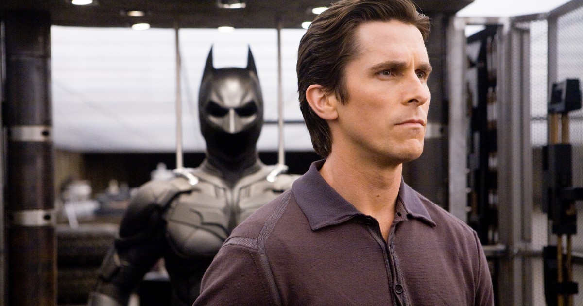 Primo piano di Bruce Wayne con alle spalle il costume di Batman - nerdface