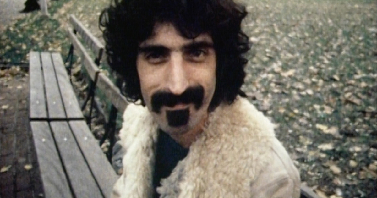 un primo piano di zappa seduto su una panchina e con un'espressione buffa - nerdface