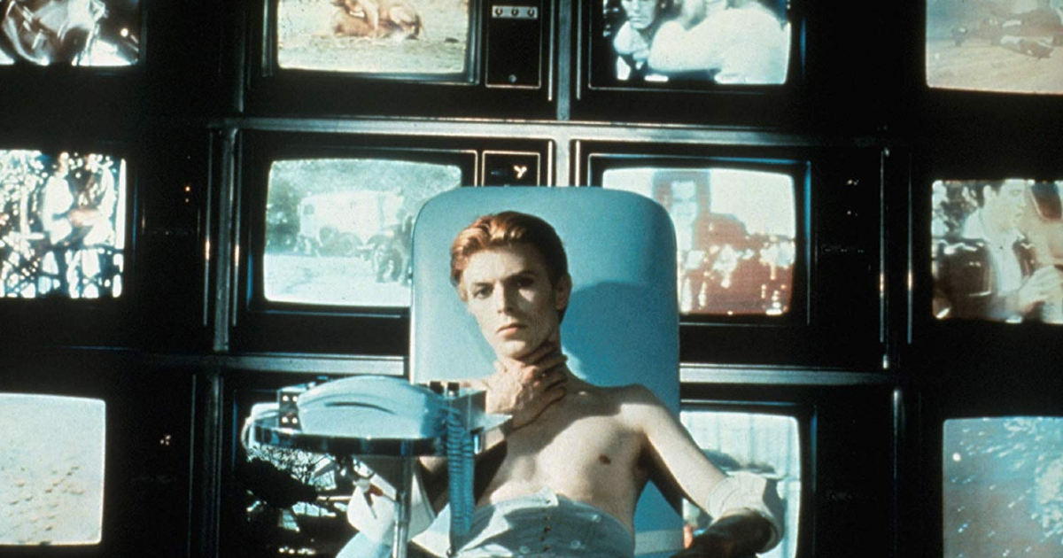 david bowie a petto nudo è seduto e dietro lui c'è un muro di schermi televisivi - nerdface