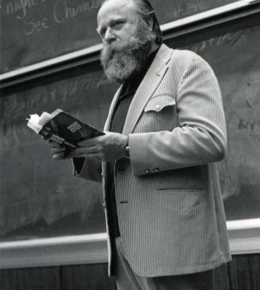 frank herbert in piedi legge un libro in un'aula - nerdface