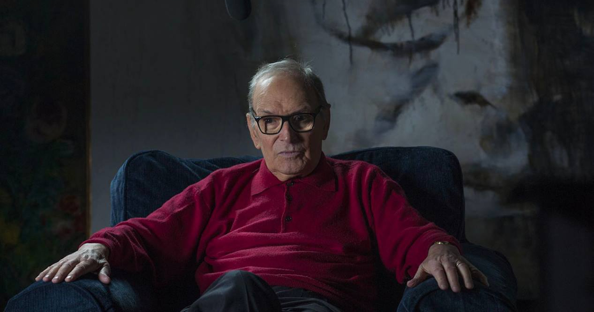 ennio morricone in maglio rosso è seduto su una poltrona - nerdface