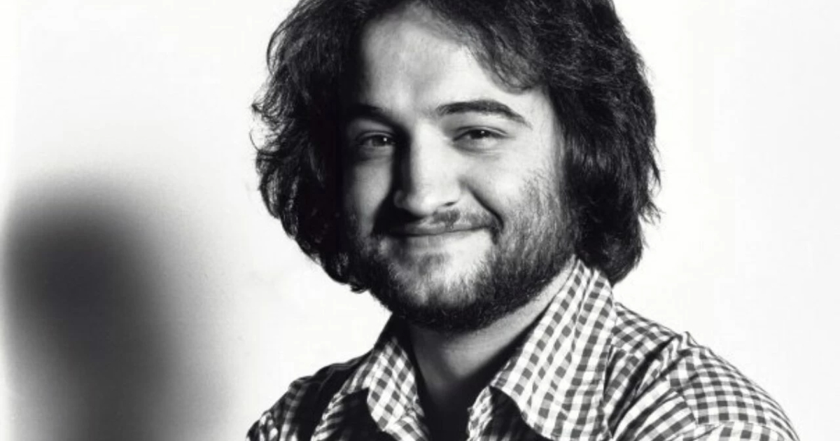 un giovane john belushi con capelli lunghi e barba sorride - nerdface