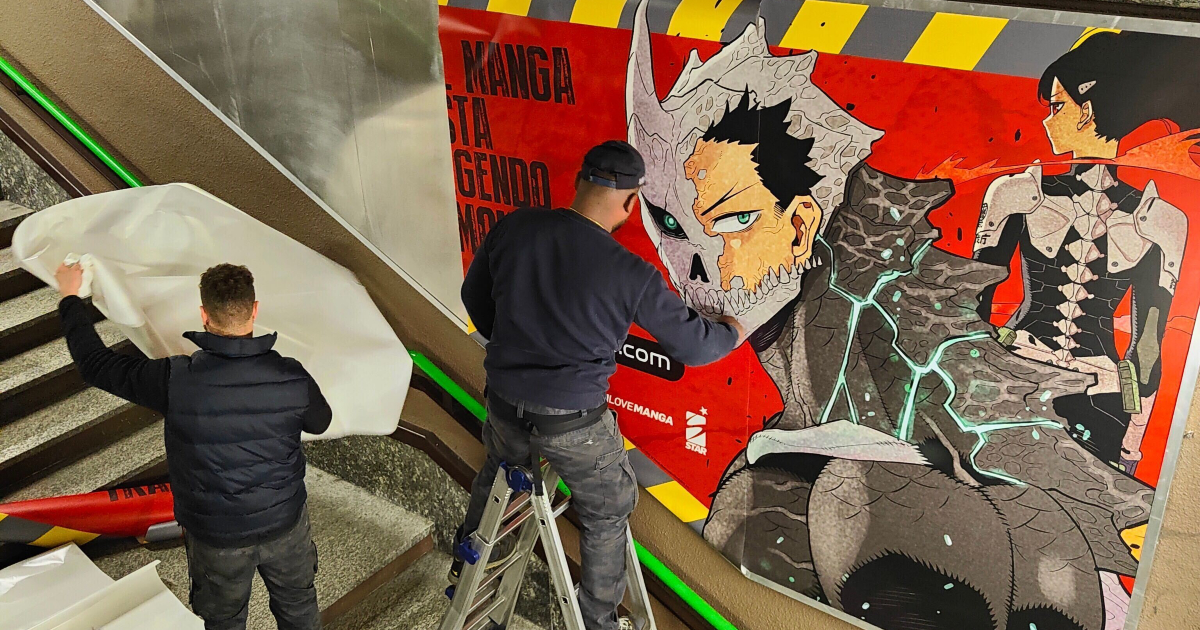 due uomini affiggono un grande poster di kaiju no 8 in metropolitana - nerdface