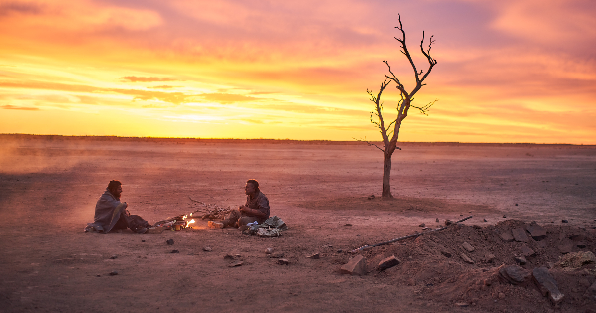 Anthony Hayes e Zac Efron sono seduti davanti ad un falò nel deserto in un'immagine di gold - nerdface