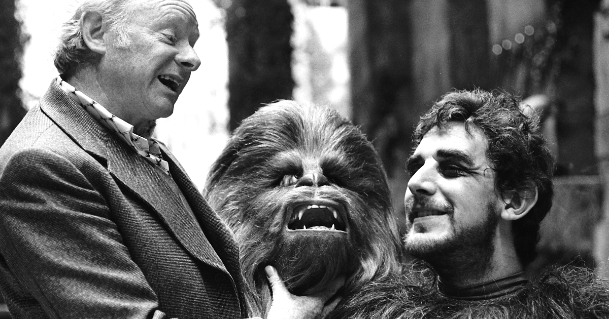 un giovane peter mayhew riceve la maschera di chewie da un uomo e sorride - nerdface