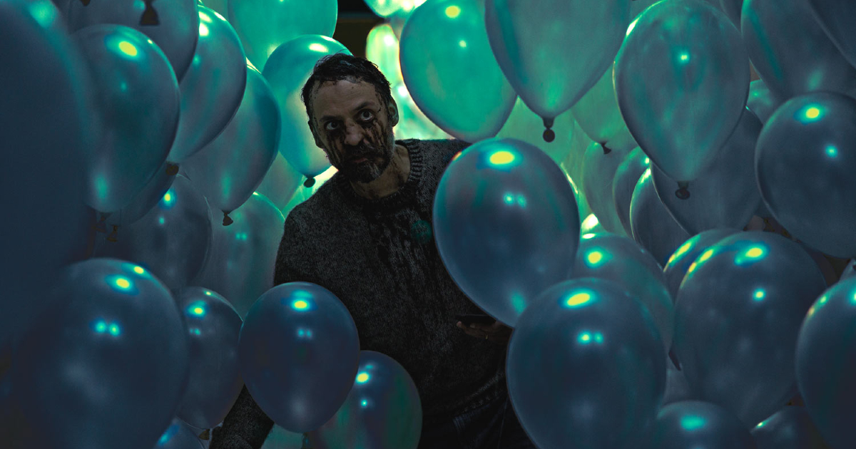 un uomo si aggira in mezzo a decine di palloncini in piove - nerdface