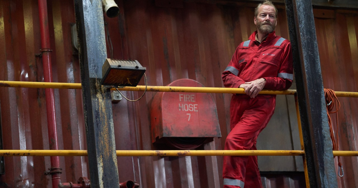 iain glenn poggiato su una balaustra in the rig - nerdface