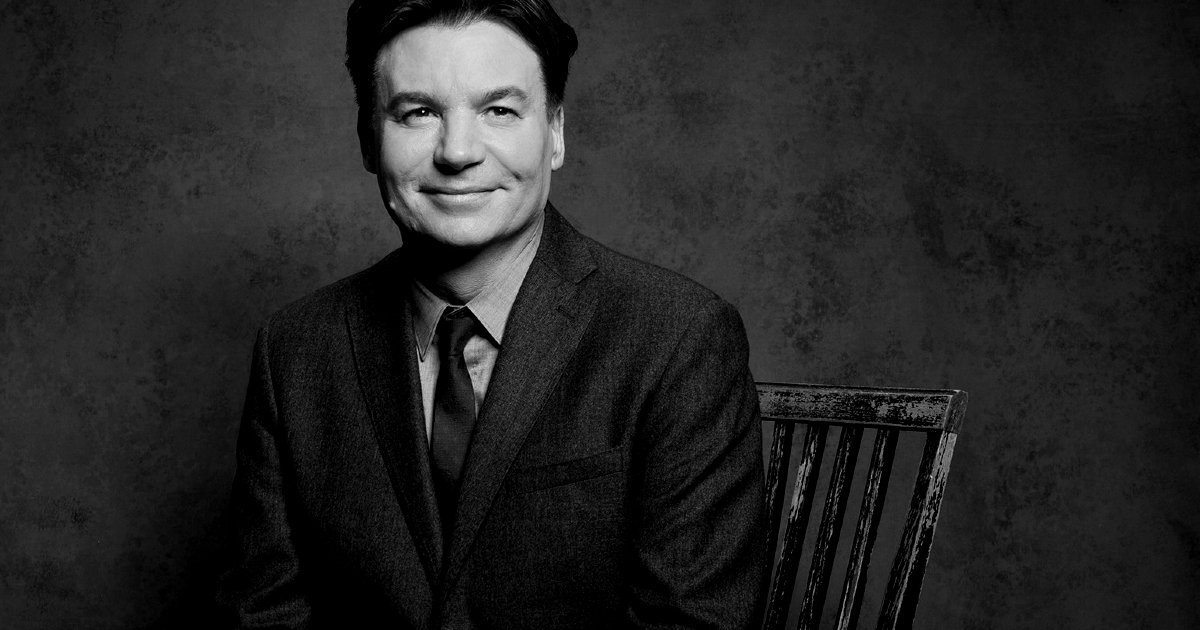 mike myers è seduto su una sedia e sorride - nerdface