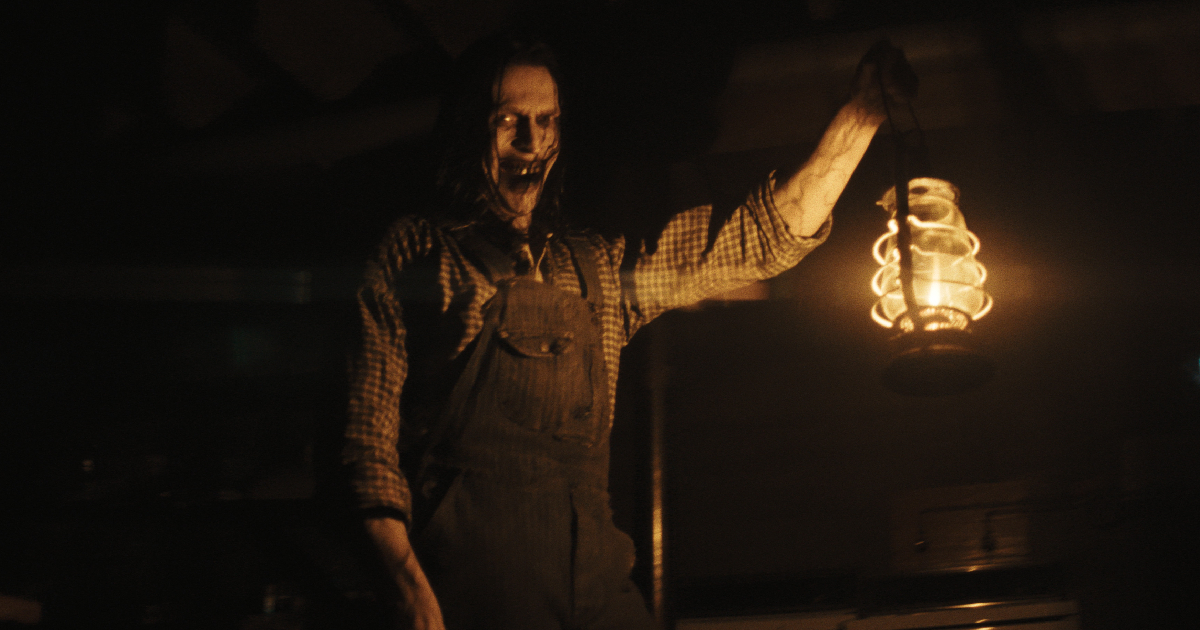 un uomo mostruoso sogghigna e tiene una lampada in the conjuring il rito finale - nerdface