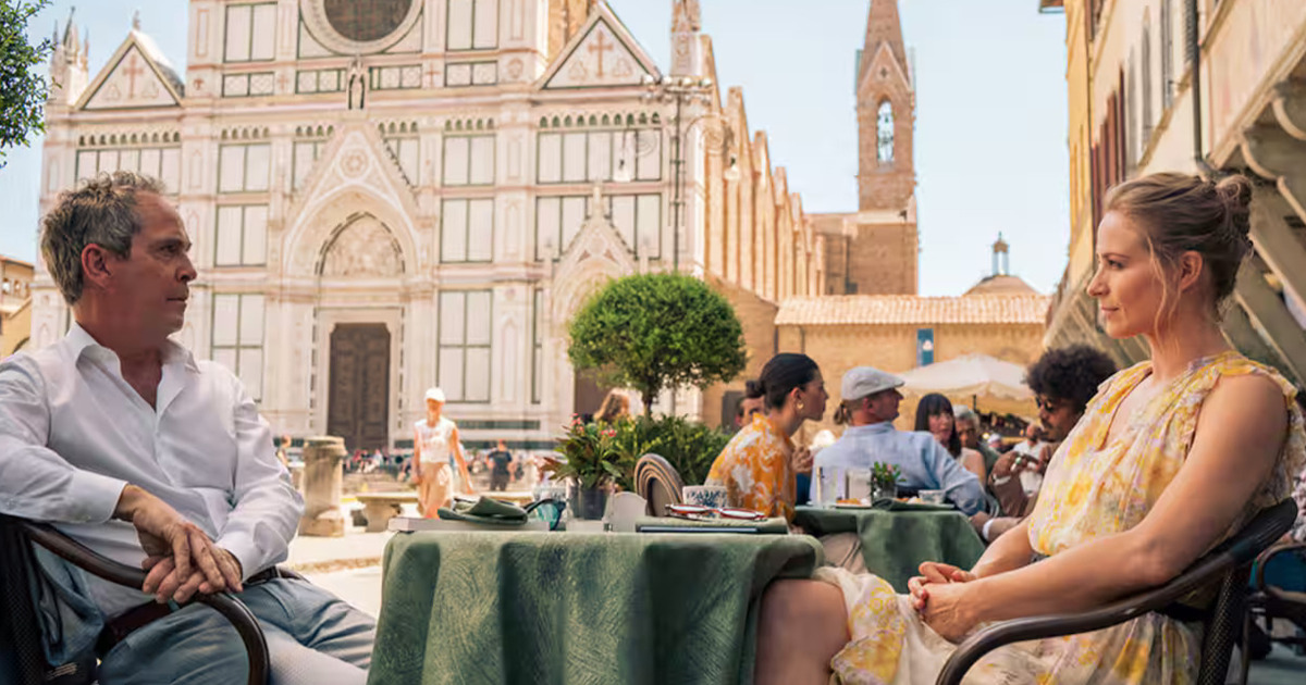 i due protagonisti seduti a un tavolino in una piazza davanti una chiesa - nerdface