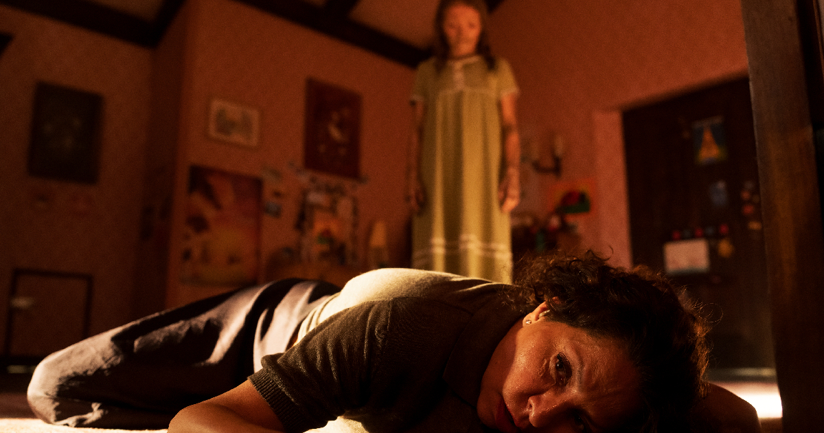 la bambina posseduta osserva una donna stesa a terra in lee cronin la mummia - nerdface